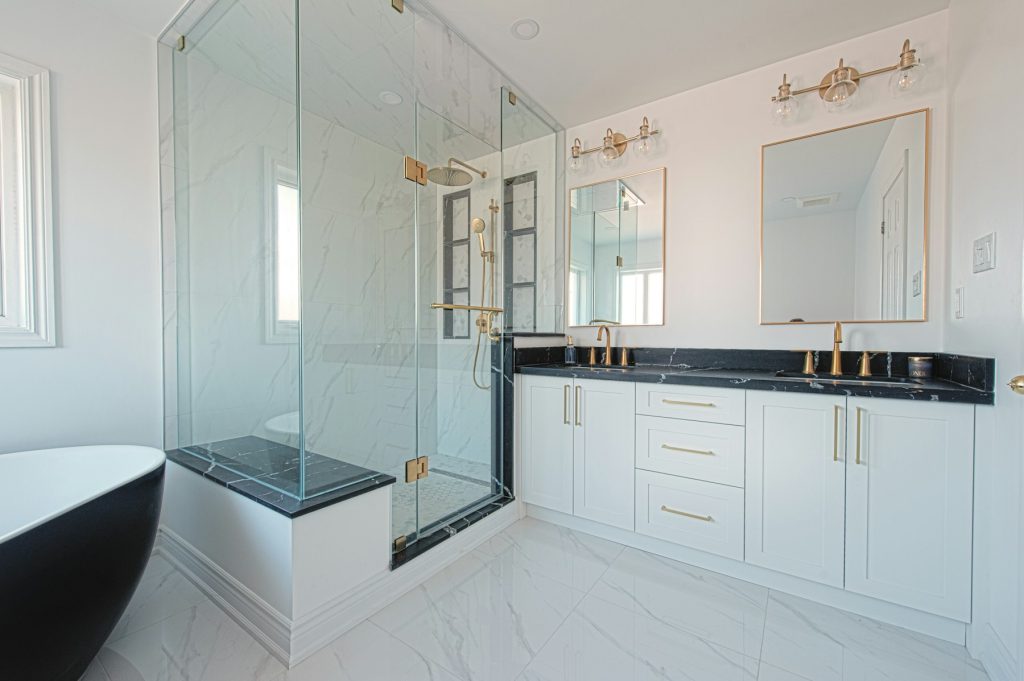 Remodeled bathroom with a glass shower, brass fixtures, double vanity and black freestanding tub