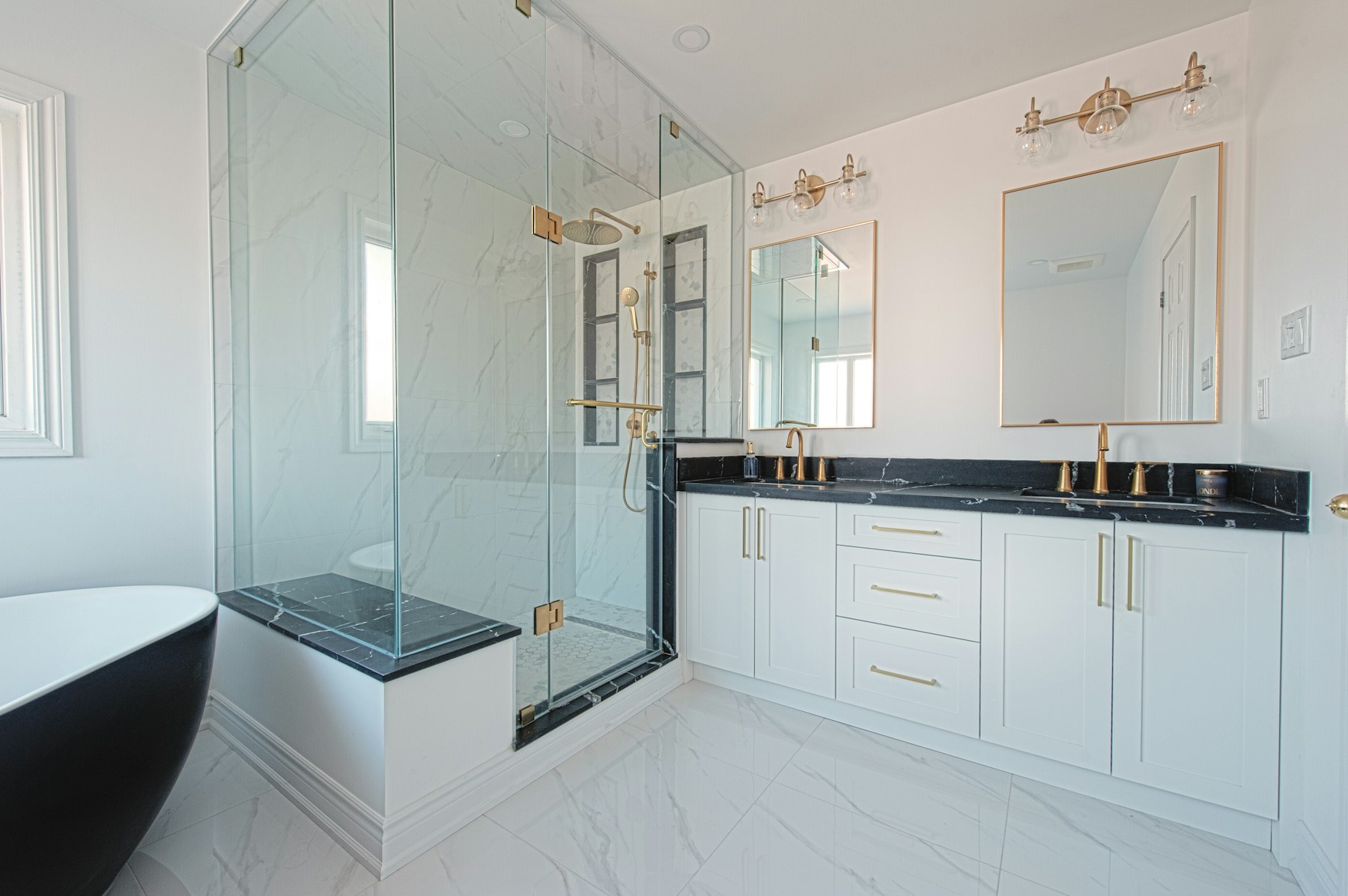 Remodeled bathroom with a glass shower, brass fixtures, double vanity and black freestanding tub