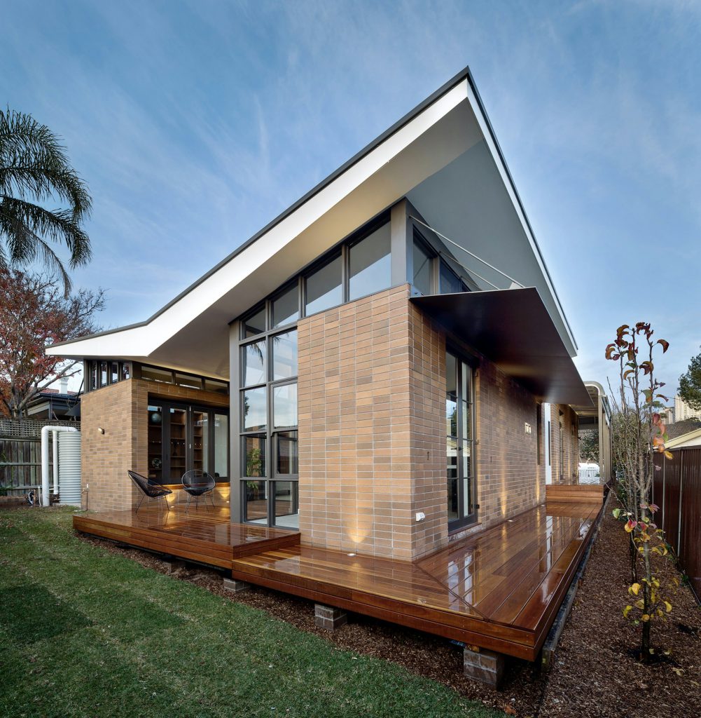 Modern home addition with a shed roof, tall glass walls and a wraparound wood deck